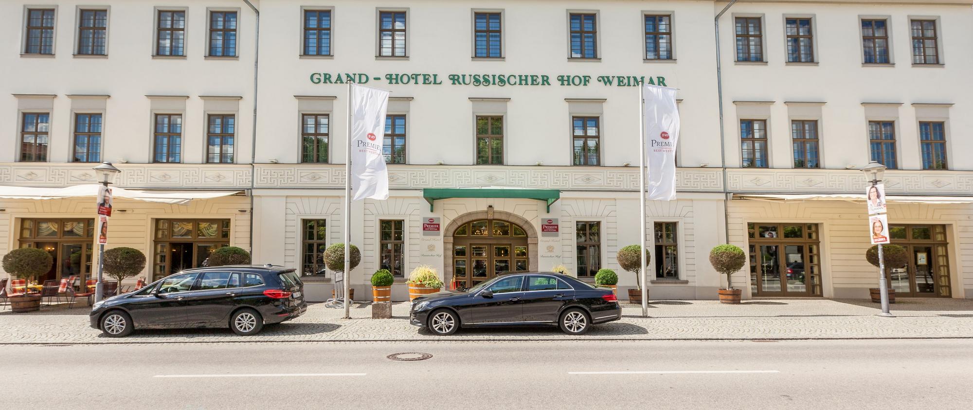 Fassade des Grand Hotel Russischer Hof Weimar mit klassischer Architektur, grüner Markise, Flaggen und geparkten Autos.